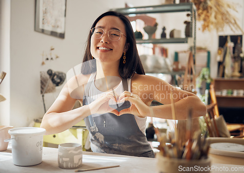 Image of Happy woman, portrait or heart hand gesture in pottery studio, Asian small business or creative ceramic workshop. Smile, clay or art mud worker in love, support or trust vote of startup store success