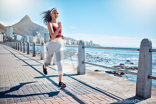 Image of Woman running at ocean promenade for fitness, energy and strong body in Cape Town. Female runner, sports person and athlete at seaside for marathon, cardio exercise and healthy summer workout in sun