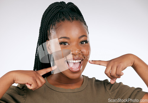 Image of Portrait, dental and a black woman pointing to her mouth in studio on a gray background for oral hygiene. Face, teeth and an attractive young female inside to point at her teeth for whitening