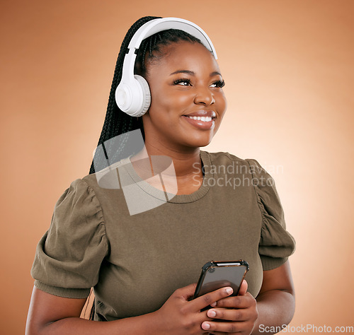 Image of Black woman, phone and headphones with smile for music or entertainment against a studio background. Happy African American female smiling in joyful happiness listening or streaming audio track