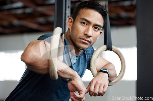 Image of Portrait, gymnastic rings and olympics with a man gymnast hanging on equipment for workout in gym. Face, fitness and exercise with a male athlete training in gymnastics for health or power