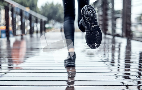 Image of Runner training in the rain, person doing workout and outdoor cardio for marathon race in Seattle road. Shoes splash water in puddle, step on wet ground and legs moving fast for fitness exercise