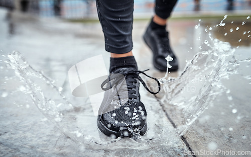 Image of Shoes of person running in the rain, feet splash water in puddle and outdoor cardio in Seattle road. Runner training for marathon, step on wet ground and legs moving fast for fitness exercise