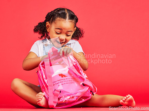 Image of School, bag and red background with a student black girl in studio sitting on the floor against a wall. Children, education and excited with a female kid pupil getting ready for learning, or growth