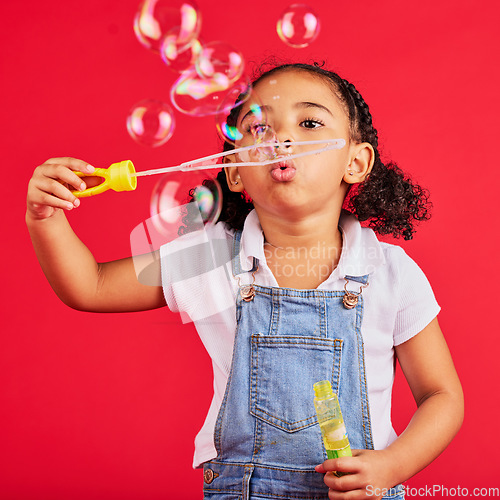 Image of Little girl, playing or blowing bubbles on isolated red background in hand eye coordination, activity or fun game. Child, kid or youth with soap, wand or toy in studio for breathing development skill