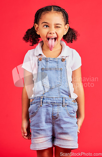 Image of Child, face and tongue out on isolated red background in goofy, silly games and playful facial expression. Happy, kid and funny little girl with comic, emoji and winking charades in studio activity