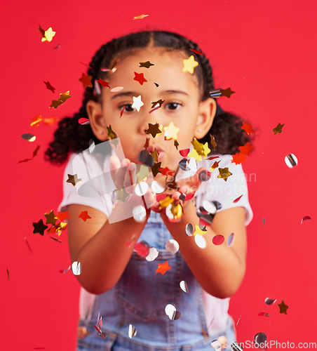 Image of Young girl, kid blowing confetti with party and celebration, gold and glitter isolated against red background. Fun, youth and child at event, celebrate and birthday in studio with decoration