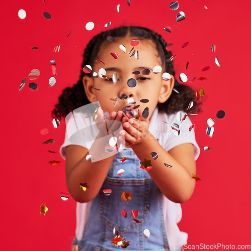 Image of Young girl, child blowing confetti with party and celebration, silver and glitter isolated against red background. Fun, youth and kid at event, celebrate and birthday in studio with decoration