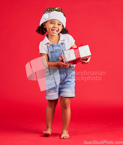 Image of Portrait, christmas and gift with a black girl on a red background in studio for festive celebration. Box, present and kids with a happy female child celebrating a holiday tradition in december