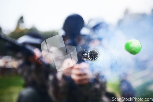 Image of Paintball, shooting and person with a gun during a game, competition or match on a field. Fire, smoke and tool in motion for attack, battle and aim with a weapon during an outdoor cardio sport