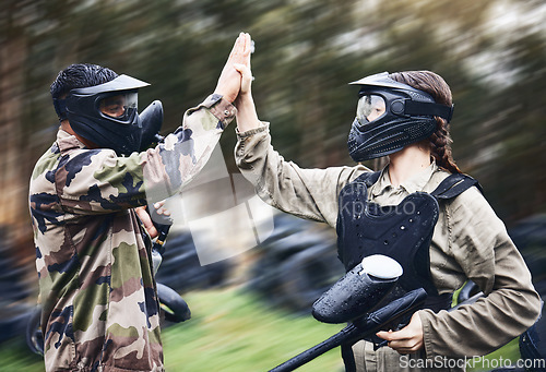 Image of Paintball, team and high five for winning victory, achievement or successful game time on the field. Man and woman in celebration for war win in extreme sports together and touching hands in teamwork