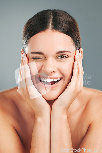 Image of Beauty, wellness and portrait of woman wink on gray background for cosmetics, facial treatment and spa. Dermatology, skincare and face of happy girl for glow, healthy skin and natural smile in studio