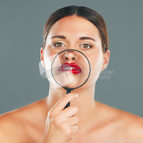 Image of Portrait, magnifying glass and lips with a model woman in studio on a gray background for red makeup. Face, cosmetics or search with an attractive and funny young female checking her skin