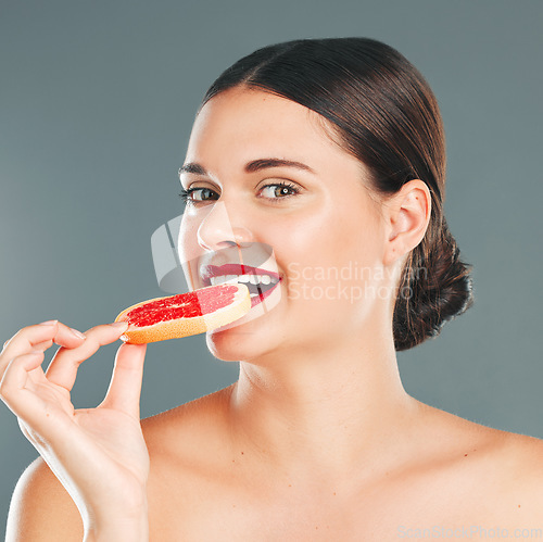 Image of Fruit bite, portrait and woman eating a grapefruit for nature and wellness aesthetic in a studio. Model, beauty and natural skincare of a young person with red lipstick hungry for vitamin c nutrition