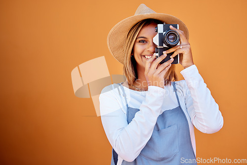 Image of Photographer, portrait and woman shooting a picture or photo with a retro camera isolated in an orange background. Happy, studio and female taking creative shots or fashion photographs as photography