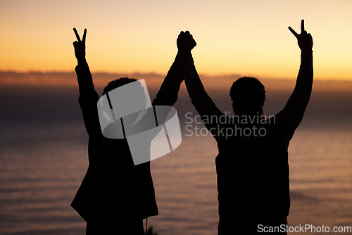 Image of Sunset, beach and silhouette of couple celebration, success or winning and holding hands in shadow, night or dark. Sky, ocean and winner people in rear with peace sign for sea, hiking or travel goals