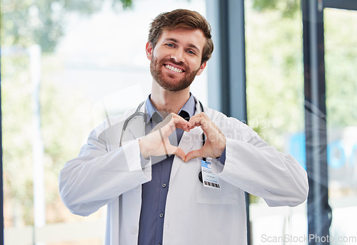 Image of Doctor, man and heart hands with smile at hospital for support, cardiology or kindness by window. Medic portrait, hand sign or medical service with icon of care, love or help for consulting at clinic