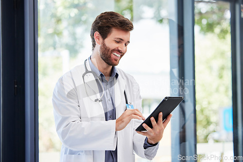 Image of Doctor, man and tablet for research at hospital for social media app, email and networking by window. Happy medic, communication or typing medical advice for help, consulting or chat on web at clinic