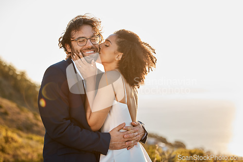 Image of Kiss, hug and wedding bride with groom for love, care and connection together in nature. Happy, partner and bond of interracial people at outdoor marriage celebration on hill in sunset.