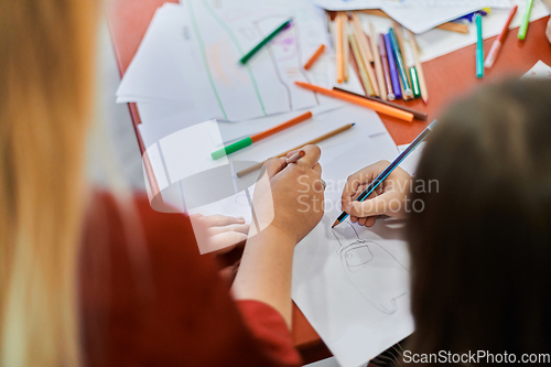 Image of Close up photo of kids during an art class in a daycare center or elementary school classroom drawing with female teacher.