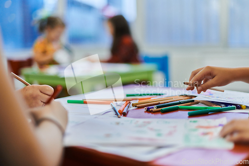 Image of Close up photo of kids during an art class in a daycare center or elementary school classroom drawing with female teacher.