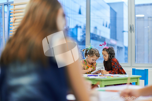 Image of Creative kids during an art class in a daycare center or elementary school classroom drawing with female teacher.