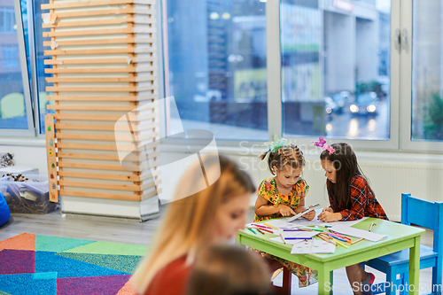 Image of Creative kids during an art class in a daycare center or elementary school classroom drawing with female teacher.