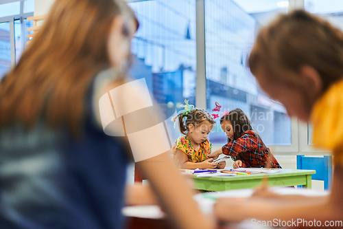 Image of Creative kids during an art class in a daycare center or elementary school classroom drawing with female teacher.