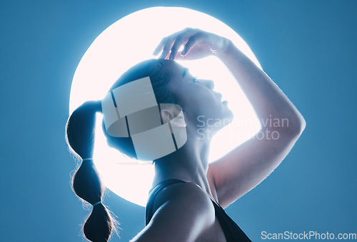 Image of Beauty, light and profile of a model in a studio with a sensual, soft and attractive pose. Cosmetic, magical and slim woman with a mystical glow posing by a moon while isolated by a blue background.