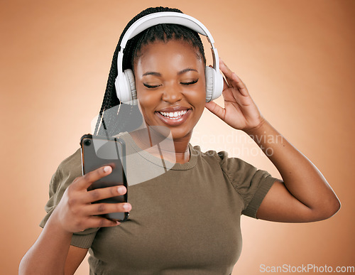 Image of Headphones, smartphone and black woman isolated on studio background for music streaming, dance and happy. Smile of african person, hand holding phone with audio technology for student subscription