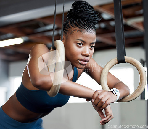 Image of Black woman, fitness and gymnastics with rings for training, muscle and arms at gym. African American female acrobat or gymnast face in strong focus for exercise, workout or practice at the gymnasium