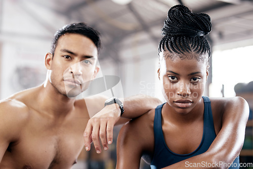 Image of Portrait, fitness and serious with a sports couple sitting in the gym together after a workout for health. Exercise, diversity and strong with a man and woman athlete sitting in a training facility
