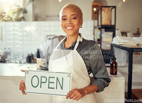 Image of Open sign, business and black woman portrait in startup cafe, restaurant or coffee shop with smile for success. Waitress, manager or person hand holding board for welcome, services and happy career