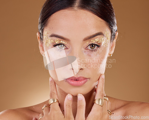 Image of Gold makeup, woman jewelry and beauty portrait with model ready for luxury skincare and spa. Brown background, studio and isolated young female person with rings, vitiligo and glitter eyes alone