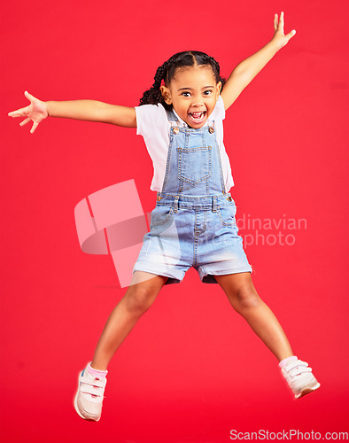 Image of Excited, playful and portrait of a girl jumping while isolated on a red background in a studio. Youth, smile and child with freedom, energy and happiness while playing with a jump on a backdrop