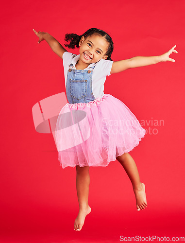 Image of Portrait, girl and jumping in tutu skirt on red background, studio and fun fashion. Happy kid, ballet clothes and energy for performance, dance and smile with happiness, ballerina dress and princess