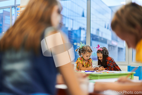 Image of Creative kids during an art class in a daycare center or elementary school classroom drawing with female teacher.