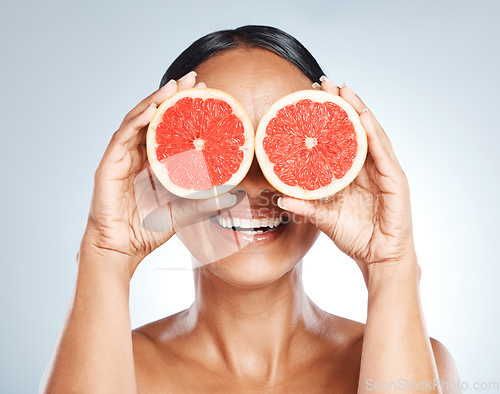 Image of Funny, fruit and woman use grapefruit for a joke covering her eyes isolated against a studio blue background. Health, beauty and skincare model smiling due to vitamin c from juicy citrus