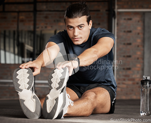 Image of Portrait, fitness and stretching with a man athlete in gym getting ready for his workout routine. Exercise, health and warm up with a handsome young male training in a performance center for wellness