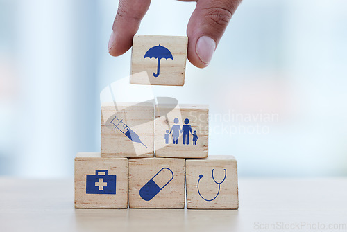 Image of Hands, wood and building blocks on table for insurance, healthcare or a safe healthy foundation. Hand of doctor putting small wooden block, object or icons with umbrella to build medical investment