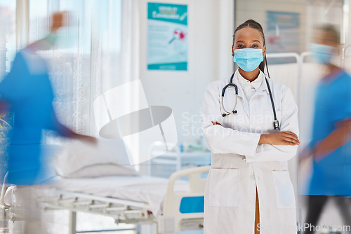 Image of Portrait, covid and healthcare with a doctor black woman arms crossed in a busy hospital for service. Trust, medical and mask with a female medicine professional working in a clinic for health