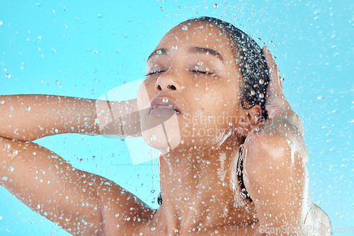 Image of Water drops, face cleaning and black woman shower with liquid for hydration, beauty healthcare or skincare hygiene. Self care studio, spa salon or relax model washing body isolated on blue background