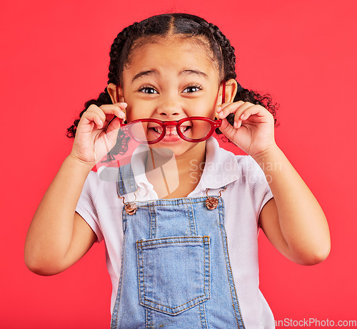 Image of Eyes, glasses in hands and portrait of child with cute smile and isolated on red background. Vision, eyesight and happy playful expression, goofy little girl holding spectacles for eyesight in studio