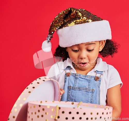 Image of Christmas, gift and girl child surprise, wow and curious in studio, happy and shock against red background. Box, present and excited toddler express omg, cheer and happiness for festive celebration