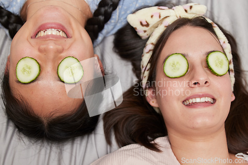Image of Friends, facial and skincare with cucumber by women relax, spa day and bonding while lying on a bed together. Beauty, girl and skin treatment with fruit, product and organic face mask in their home
