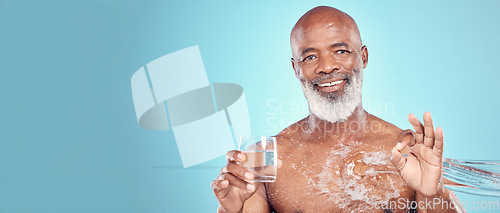 Image of Water splash, portrait and senior man in a studio with a glass of aqua and a ok hand gesture. Health, wellness and happy elderly African male with sign language by a blue background with mockup space