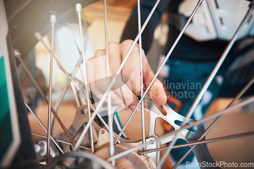 Image of Motorcycle, wheel and hands on spokes with a man at work in a repair shop or maintenance garage. Bike, mechanic and service with a professional handyman working on a bicycle rim in a workshop