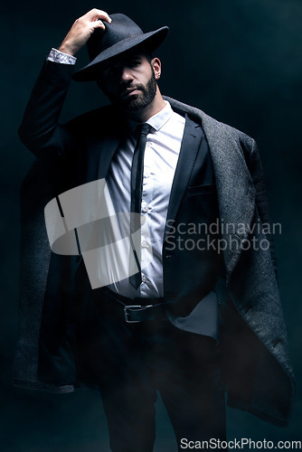 Image of Fashion, portrait and a man in a dark studio with confidence, clothes and a hat for vintage style. Model person in a suit and coat for winter, business or mystery as a spy on a black background