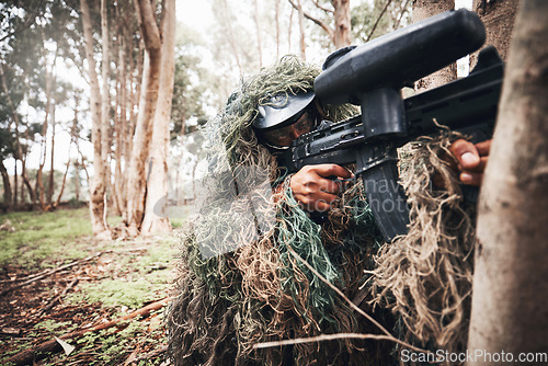 Image of Paintball gun, forrest and man with aim by trees for outdoor war game, strategy or focus in natural camouflage. Shooter, sniper and helmet for safety with eyes on target for winning in military games