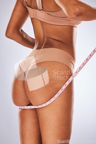 Image of Woman, butt and measuring tape in studio for weight loss, diet and health progress on grey background. Body, size and girl model check, measure and slimming results while posing in underwear isolated
